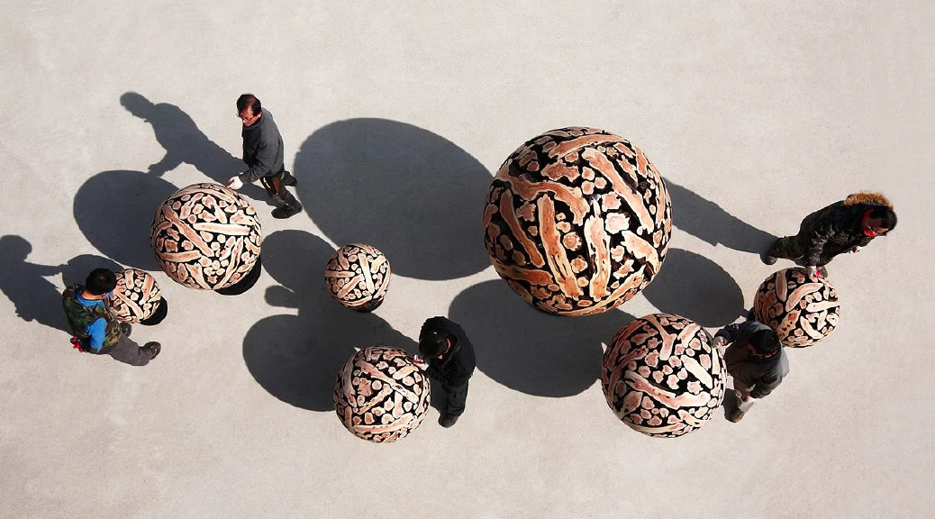 People walking around wooden spheres created by artist, Jaehyo Lee